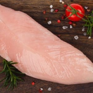 One Certified Organic, pasture raised turkey tenderloin from Wrong Direction Farm on a dark wood cutting board with salt, tomato, and rosemary.