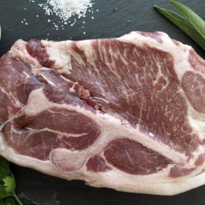 Pasture Raised pork shoulder blade steak on a slate cutting board with salt and garnishes.
