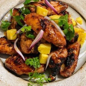 Pasture Raised and Certified Organic chicken wings barbequed served with pineapple and cilantro on a plate.