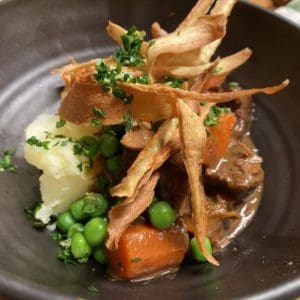 Grass fed beef stew in a bowl with crispy fried parsnips and parley gremolata garnish.