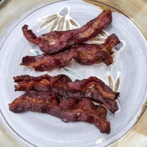 A closeup image of Wrong Direction Farm's grass fed beef bacon, cooked and on a clay plate.