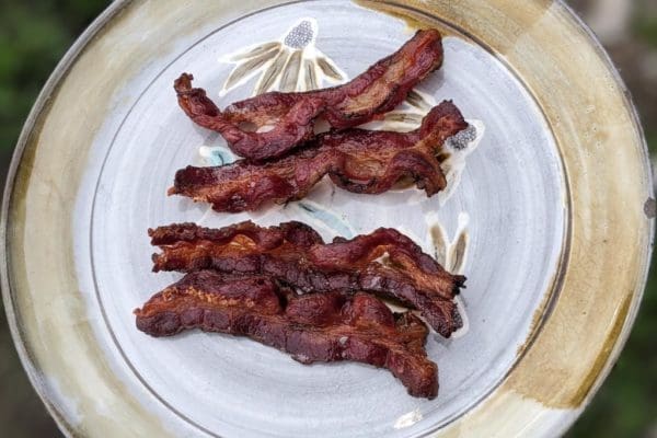 A closeup image of Wrong Direction Farm's grass fed beef bacon, cooked and on a clay plate.