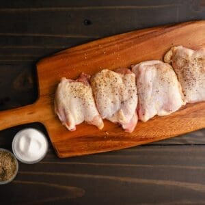 Four boneless Organic, pasture raised chicken thighs from Wrong Direction Farm n a cutting board, dusted with spices before cooking.